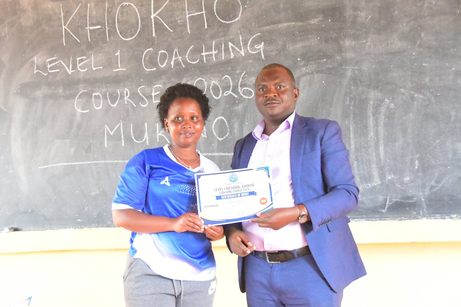 A participant receives her Level 1 coaching certificate in front of the course blackboard