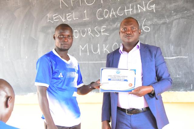 A participant receives his certificate in front of the course blackboard